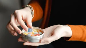 Smiling woman picking a colorful low-dose THC gummy from a small travel tin