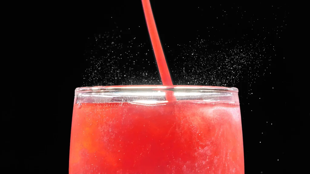 A macro close-up of a fizzy, pink nano-emulsified THC beverage with a red straw against a black background, illustrating a fast-acting cannabis drink.